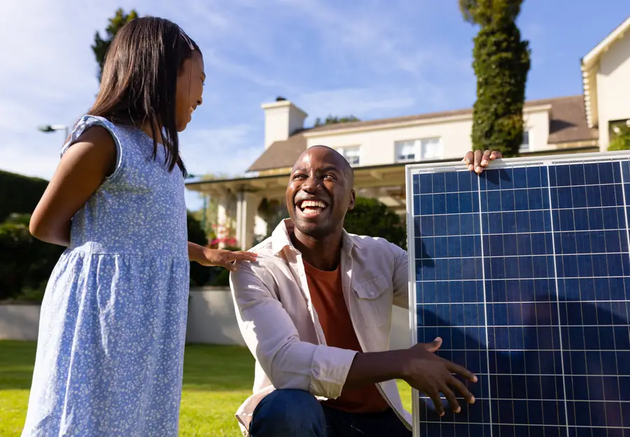 A father and daughter laughing beside a solar panel in their garden
