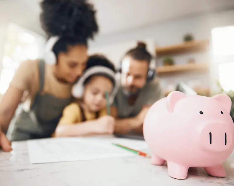 A family at the kitchen table with a piggy bank in the foreground