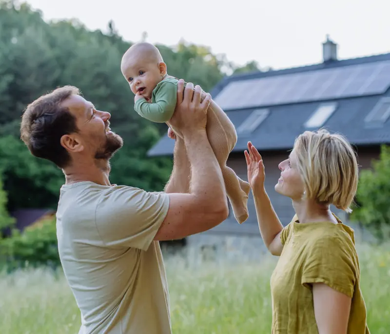 A couple playing with their baby outside a house with solar panels on the roof